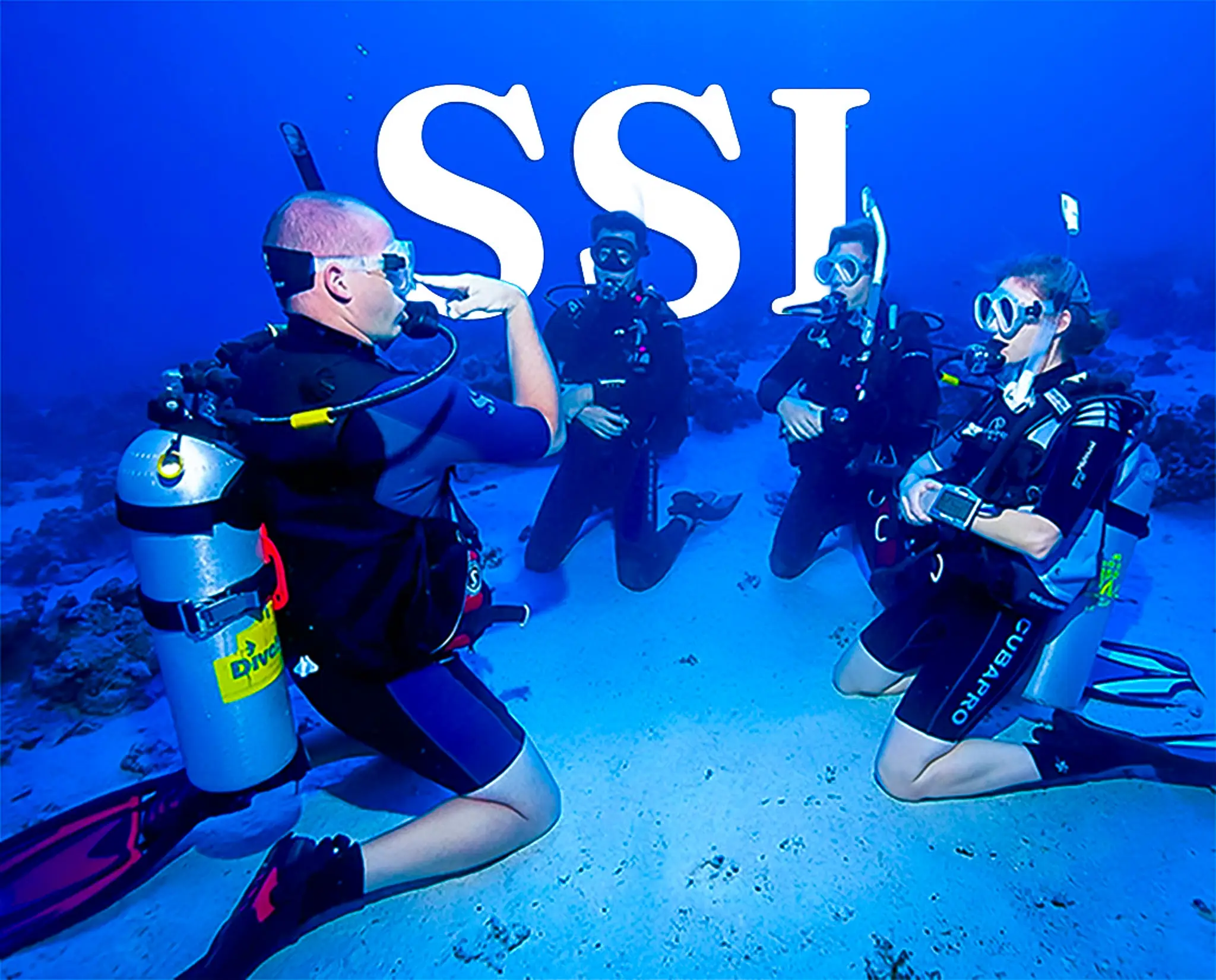 Instructor de buceo guía a tres alumnos arrodillados en el fondo marino durante una clase práctica, con el logo de SSI superpuesto.