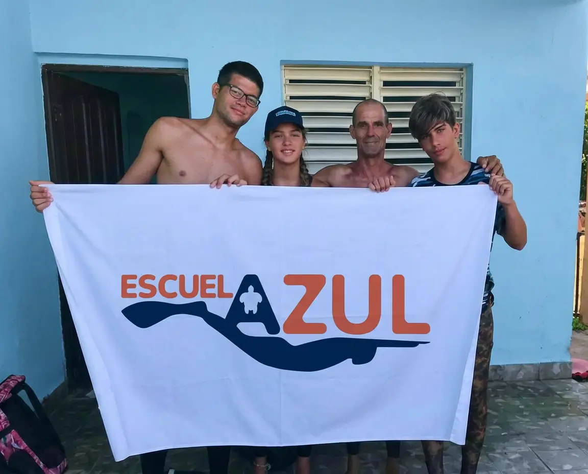 Quatre élèves de Escuela Azul posent en souriant en tenant le drapeau de l'école devant une maison bleue.